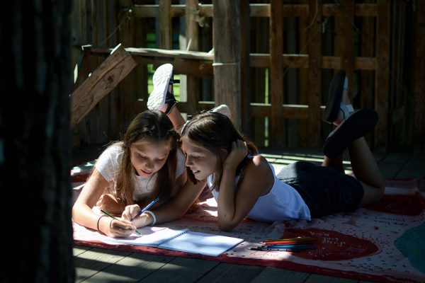 Dekleti rešujeta naloge v Otroškem potovalnem dnevniku v leseni hišici na drevesu